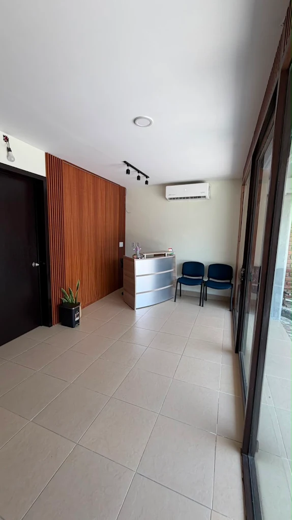 Recepción y sala de espera de Clínica Montero: mostrador, dos sillas azules, pared con listones de madera y ventanal