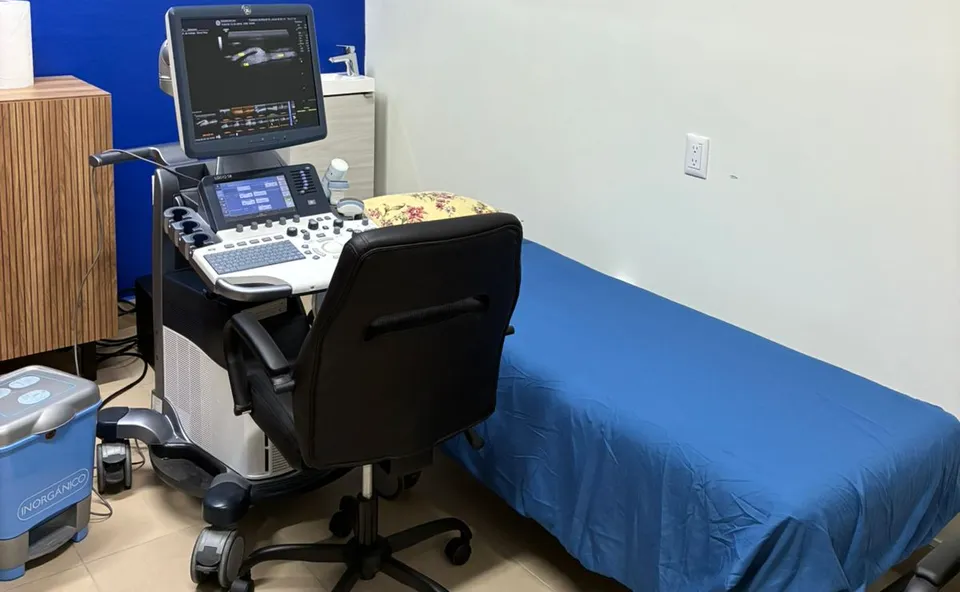 Sala de ultrasonido: equipo de ultrasonido con monitor junto a la camilla con sábana azul